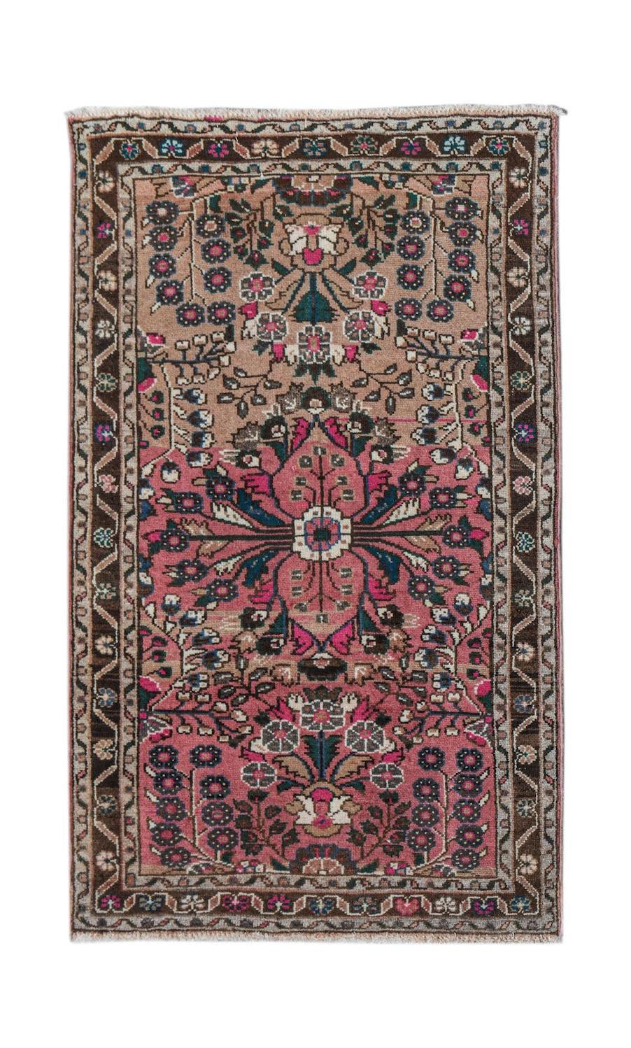 A vintage handwoven Persian Sarouk rug featuring a floral medallion on a pink and tan field.