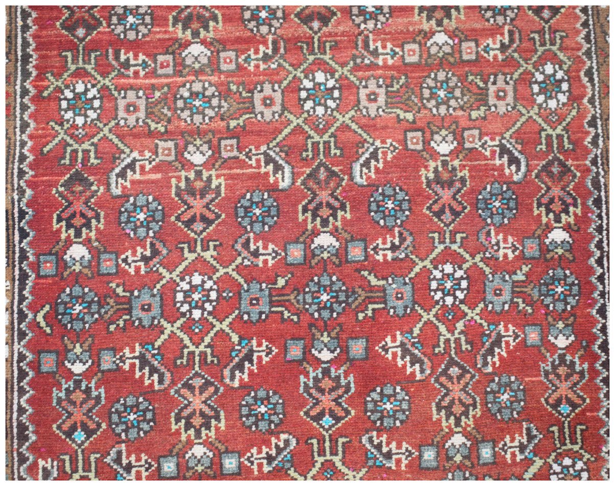 A vintage Persian Senneh runner featuring a geometric floral pattern in red, blue, and cream tones.