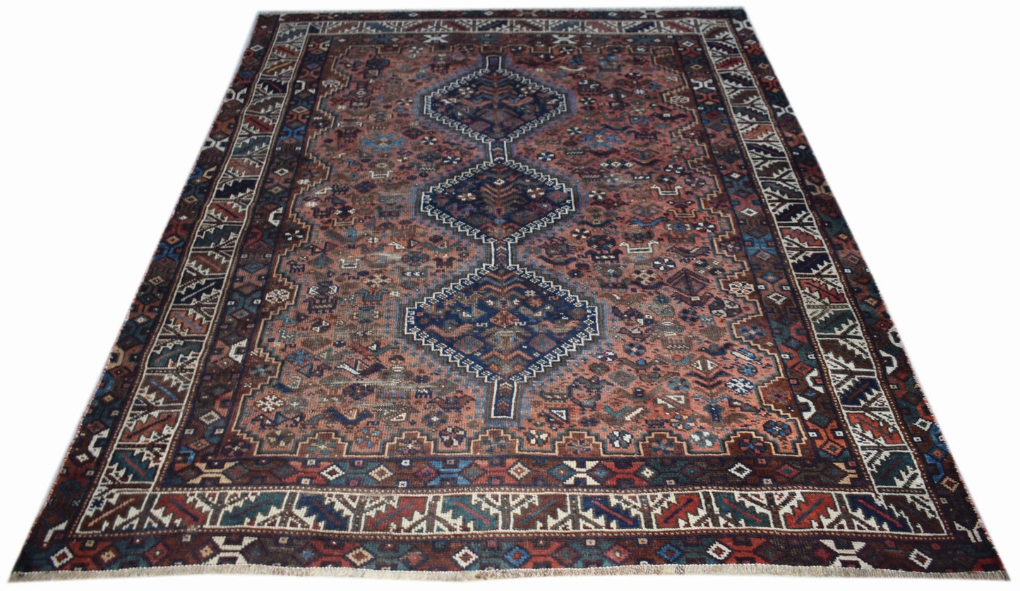 A vintage handwoven Persian Shiraz rug featuring a central diamond pattern on a reddish-brown field.