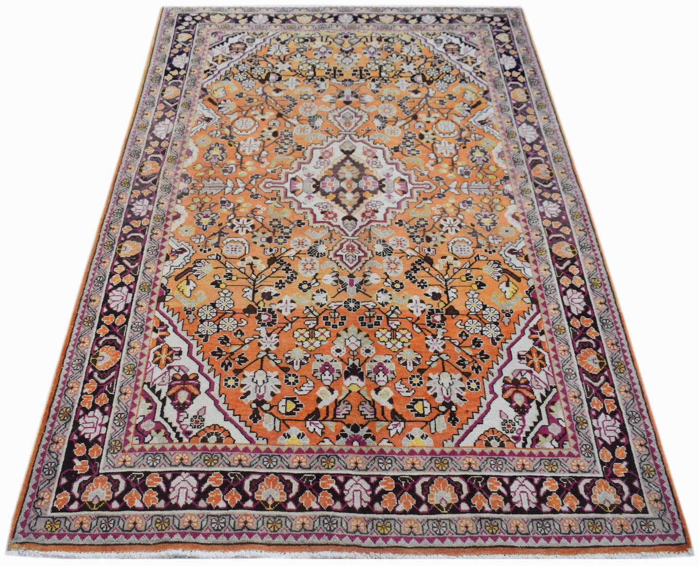 A vintage Persian Tabriz rug featuring an intricate floral pattern in orange, cream, and dark tones.
