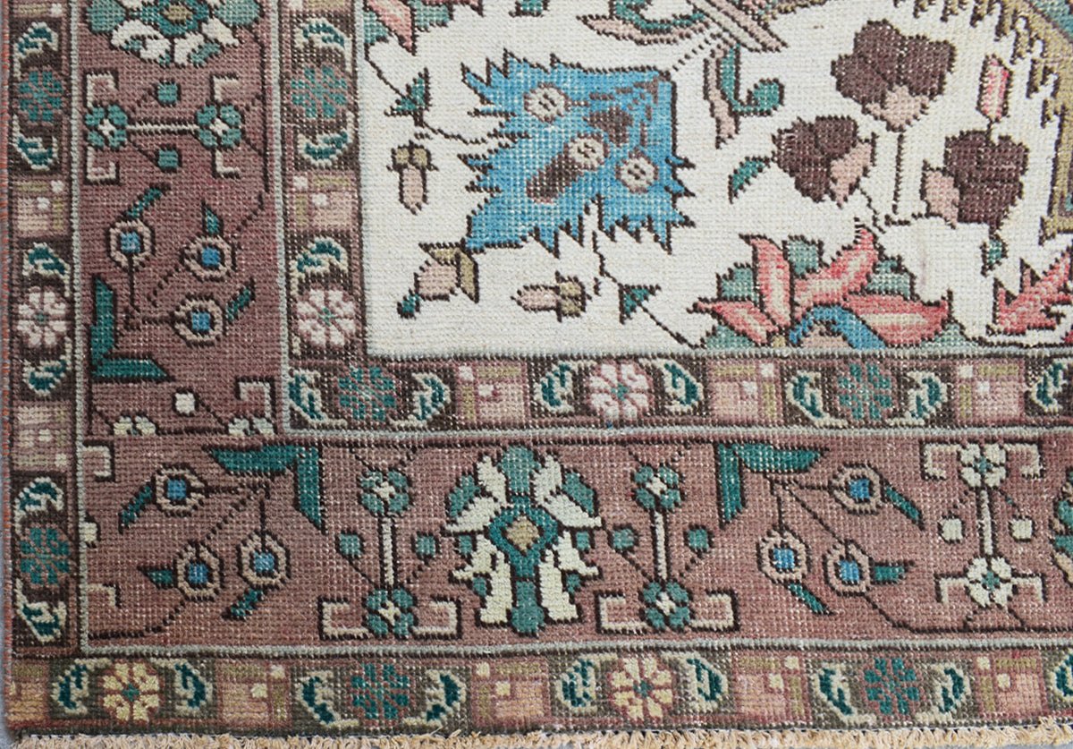 A close-up of a vintage Persian Tabriz rug featuring intricate floral patterns in muted tones.