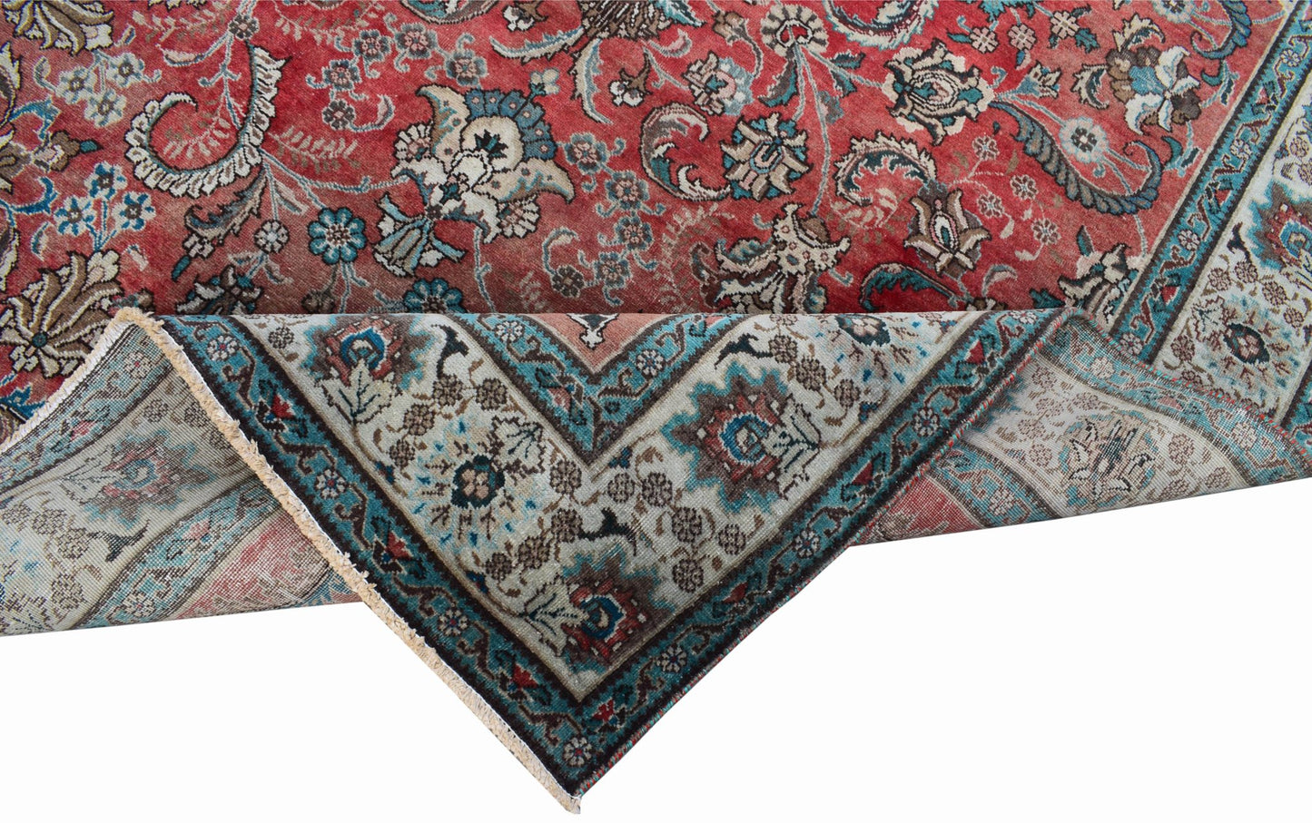 A vintage Persian Tabriz rug featuring a red field with intricate floral patterns and a folded corner.