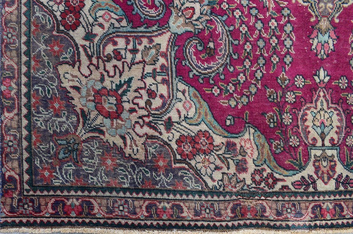 A vintage Persian Tabriz rug featuring an intricate floral pattern in magenta, cream, and blue.