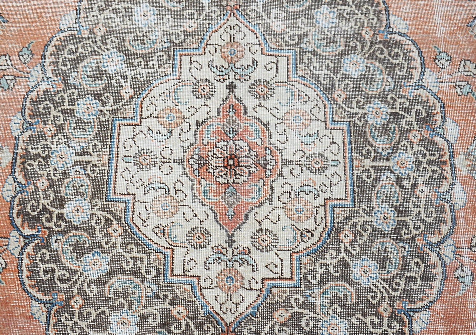 A vintage Persian Tabriz rug featuring a central floral medallion in shades of orange, blue, and grey.