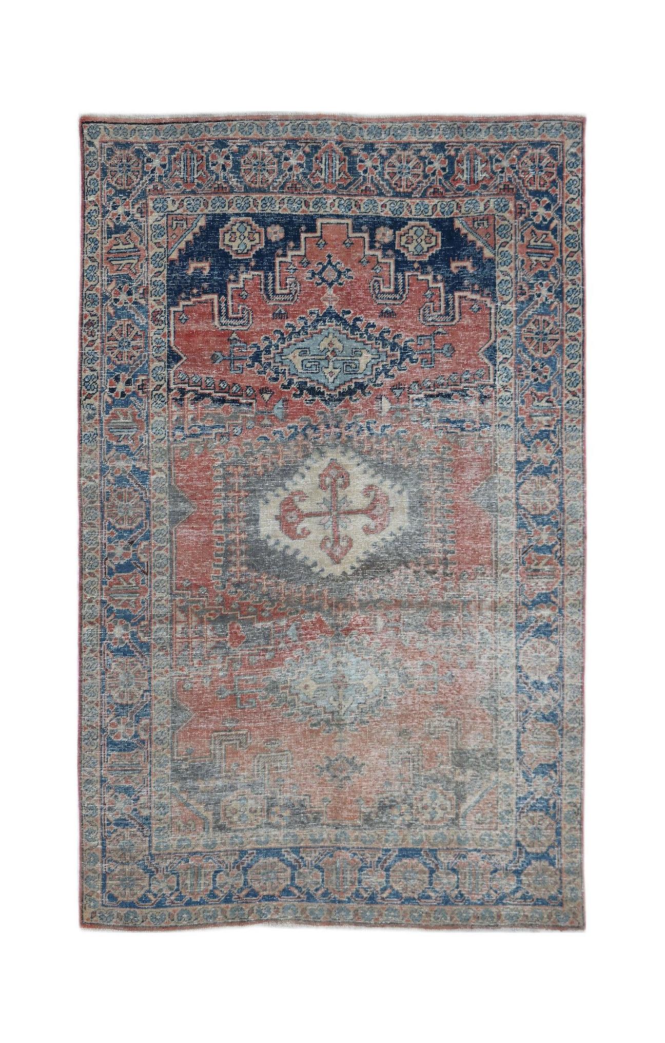 A vintage handwoven Persian wool rug featuring a faded geometric medallion in red and blue tones.