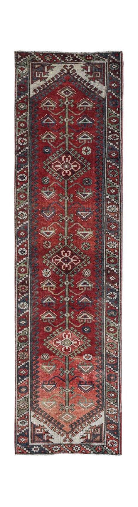 A handwoven vintage Persian runner rug featuring a red field with geometric motifs and floral stems.