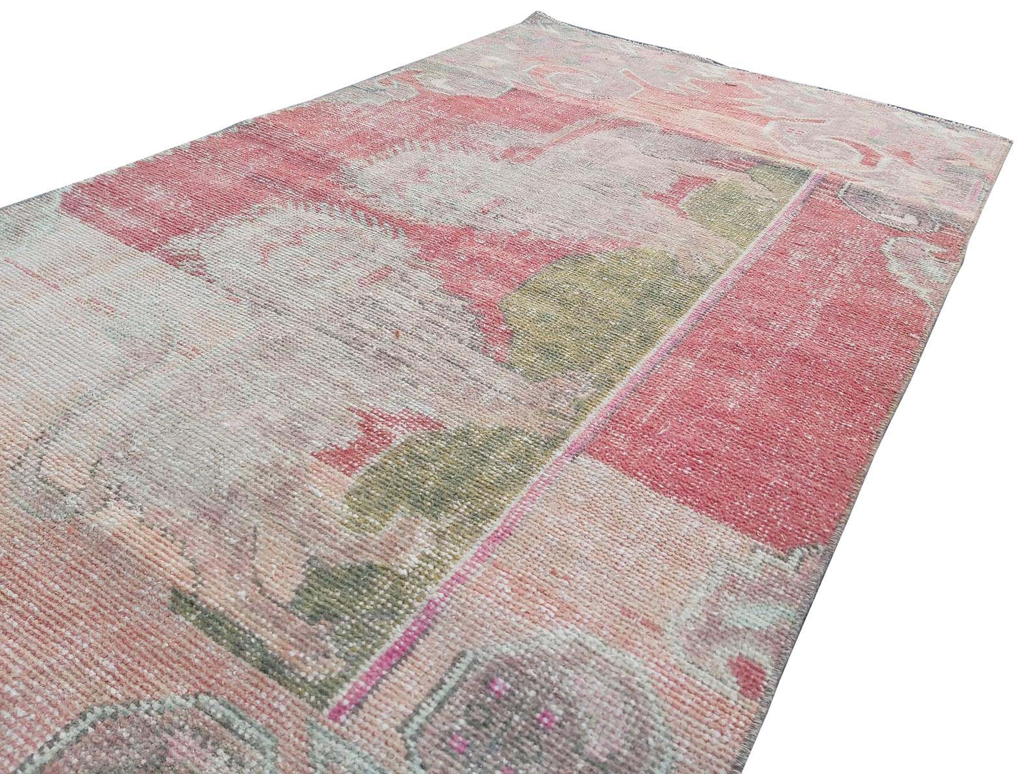A vintage handmade Turkish wool rug featuring a distressed pattern in shades of pink and green.