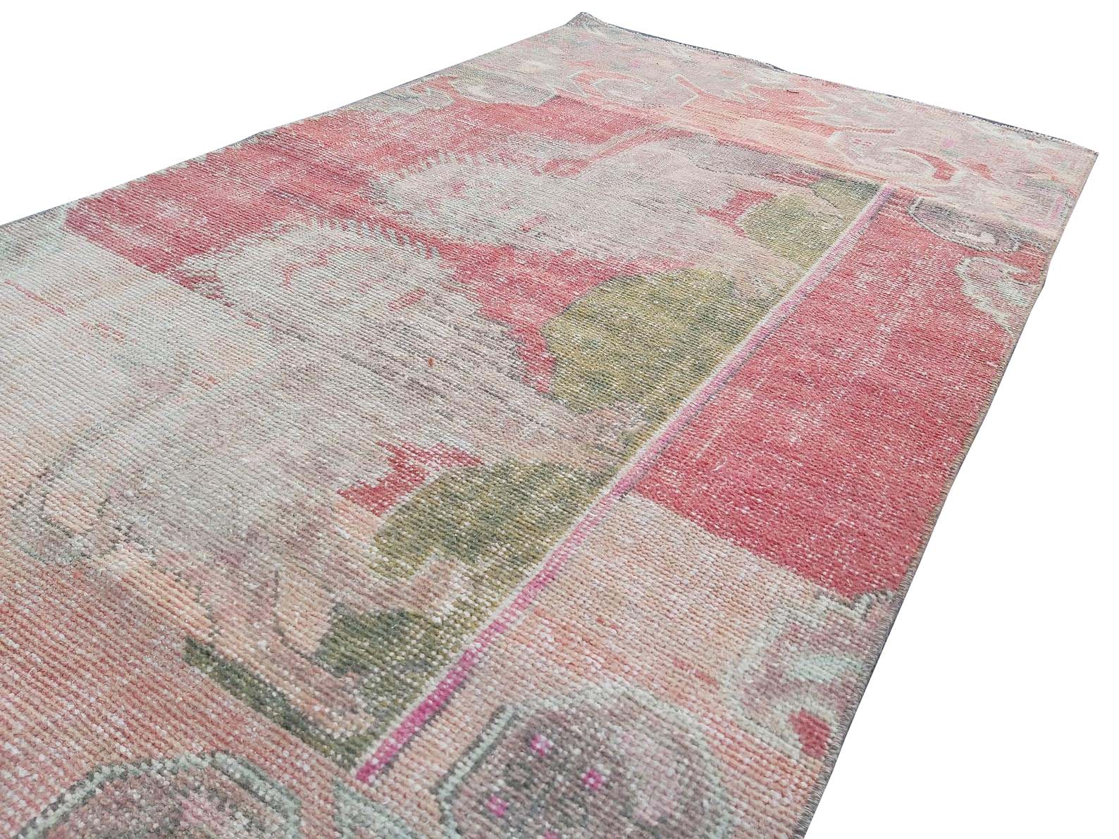 A vintage handmade Turkish wool rug featuring a distressed pattern in shades of pink and green.