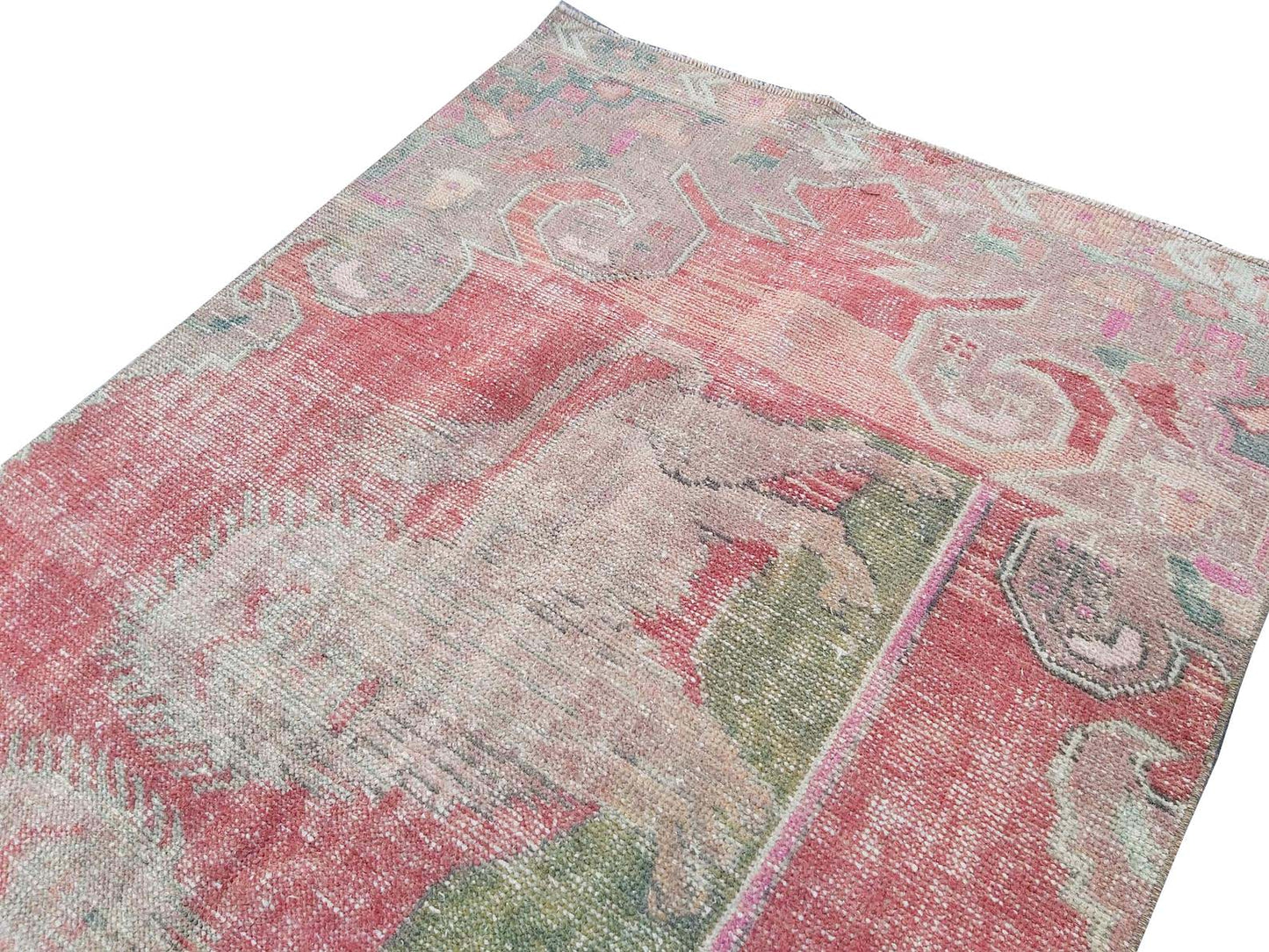 A vintage handmade Turkish wool rug featuring a faded red and green geometric pattern.