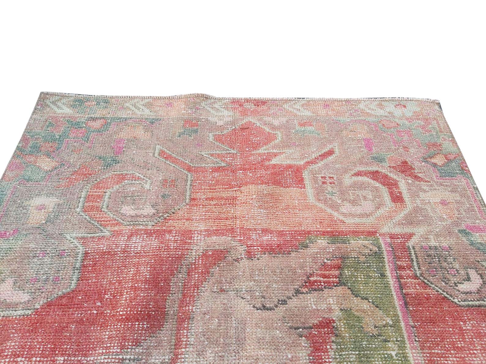 A vintage handmade Turkish wool rug featuring a faded geometric pattern in red and muted tones.