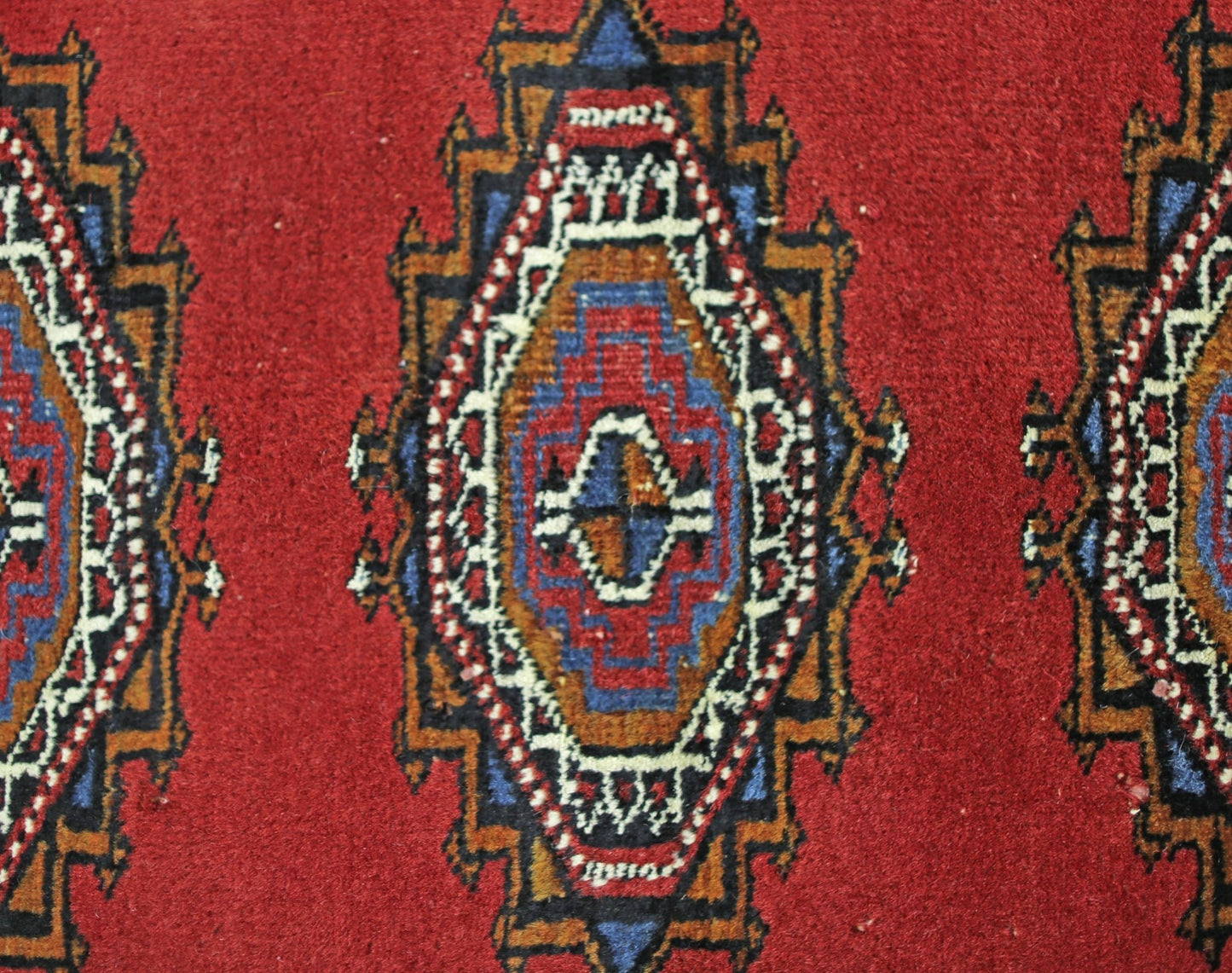 A vintage Pakistani Princess Bokhara rug featuring repeating geometric diamond motifs in red.