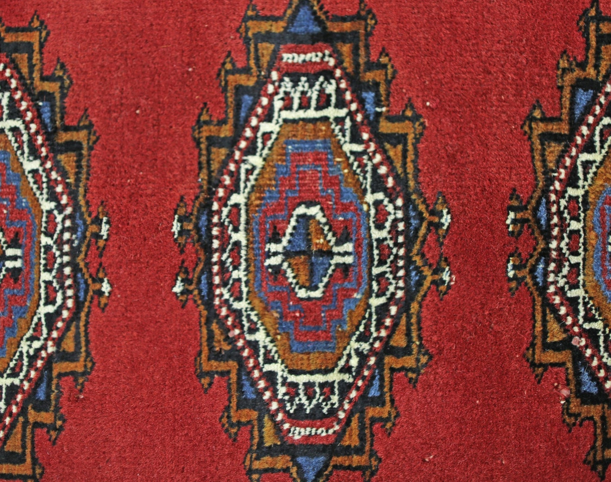 A vintage Pakistani Princess Bokhara rug featuring repeating geometric diamond motifs in red.
