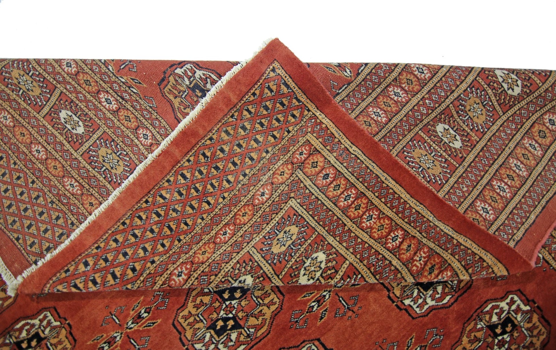 A vintage Pakistani Princess Bokhara rug with a red field and geometric patterns, shown folded.