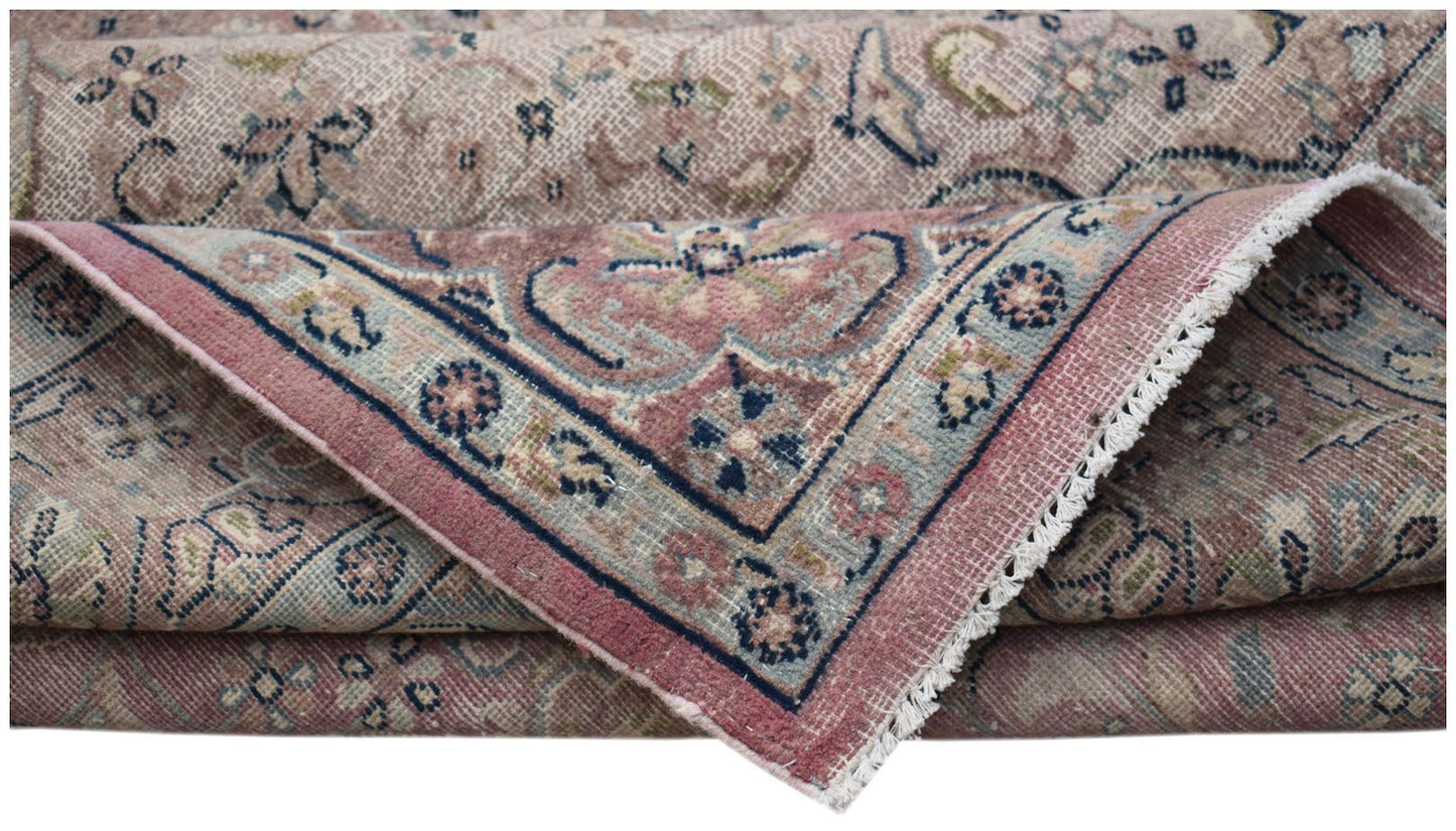 A folded vintage Persian Kerman rug featuring a floral medallion design in muted pink and blue.