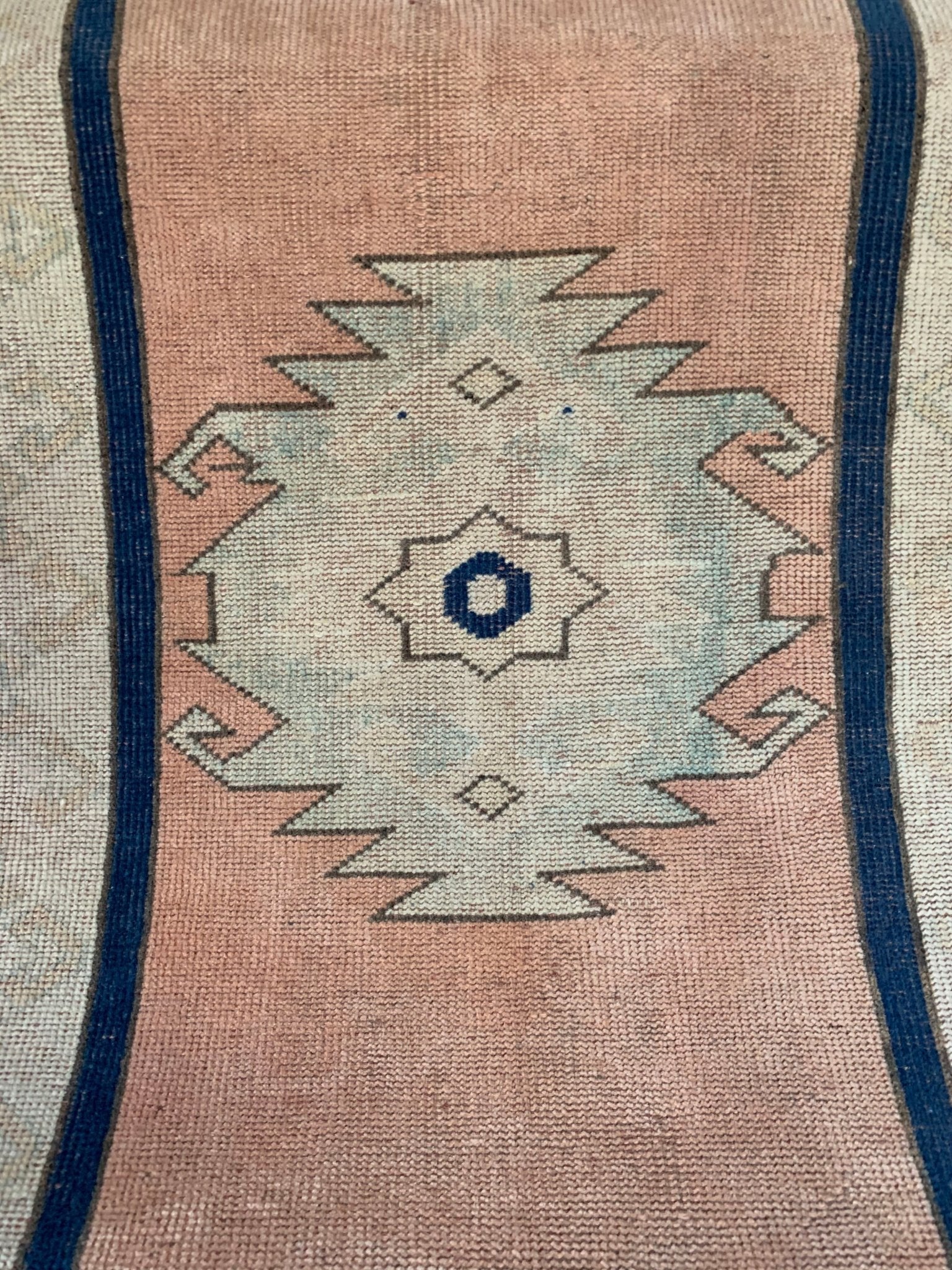 A vintage Turkish Oushak runner featuring a central tribal medallion on a soft pink background.