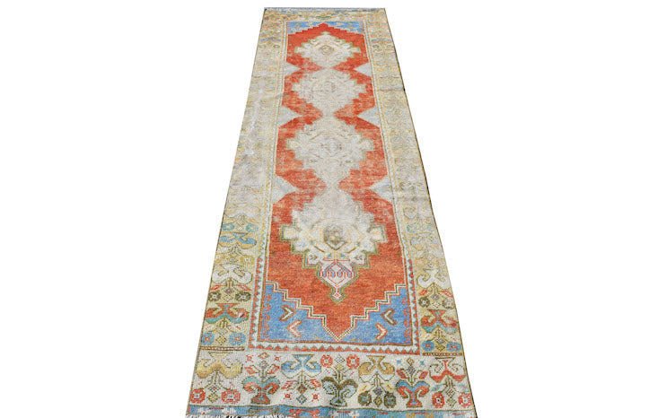 A vintage Turkish runner featuring a central orange medallion on a light field with tribal motifs.