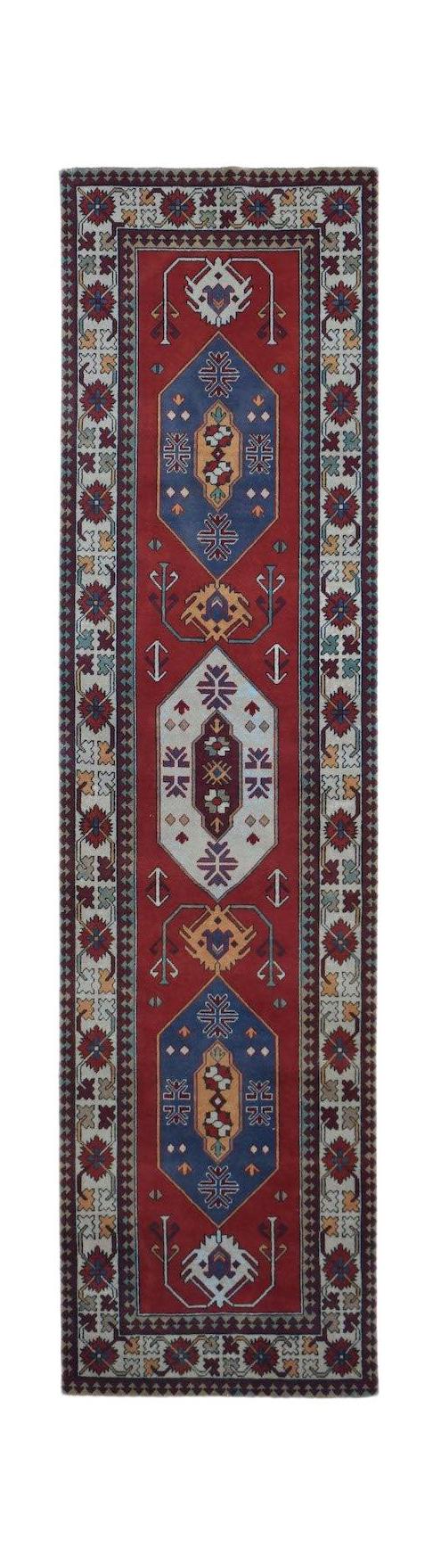 A vintage handwoven Turkish runner rug featuring geometric medallions on a red field.