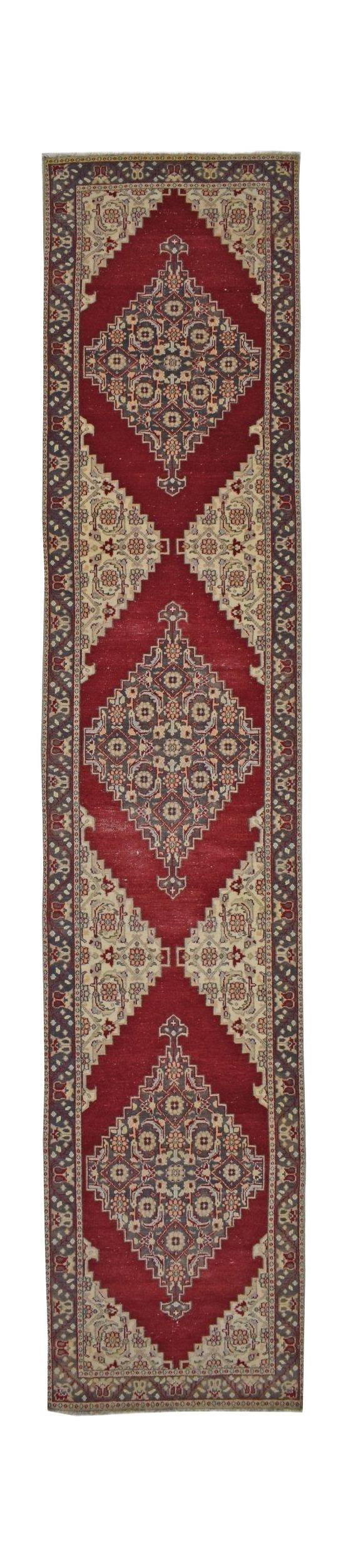 A vintage handmade Turkish runner rug featuring three central diamond medallions on a red field.
