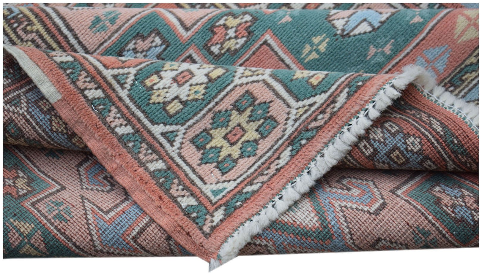 A handwoven vintage Turkish runner rug featuring geometric patterns in muted pink and teal tones.