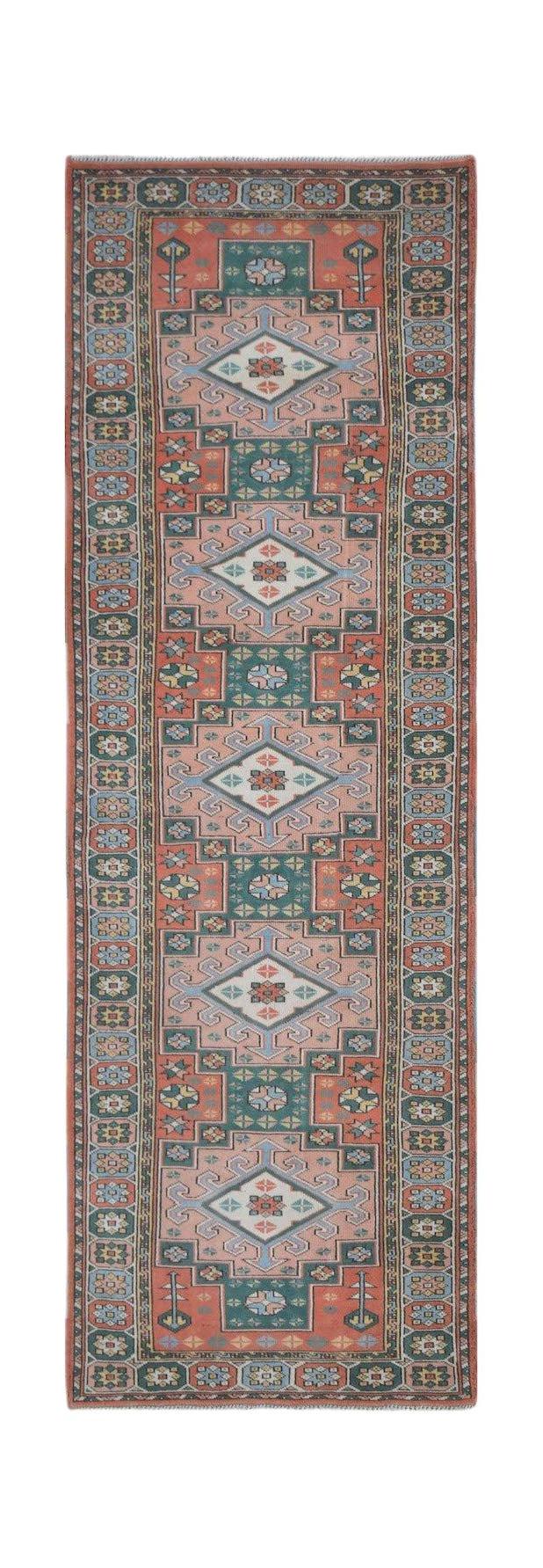 A vintage Turkish Kars runner rug featuring a geometric pattern in muted pink, blue, and green.