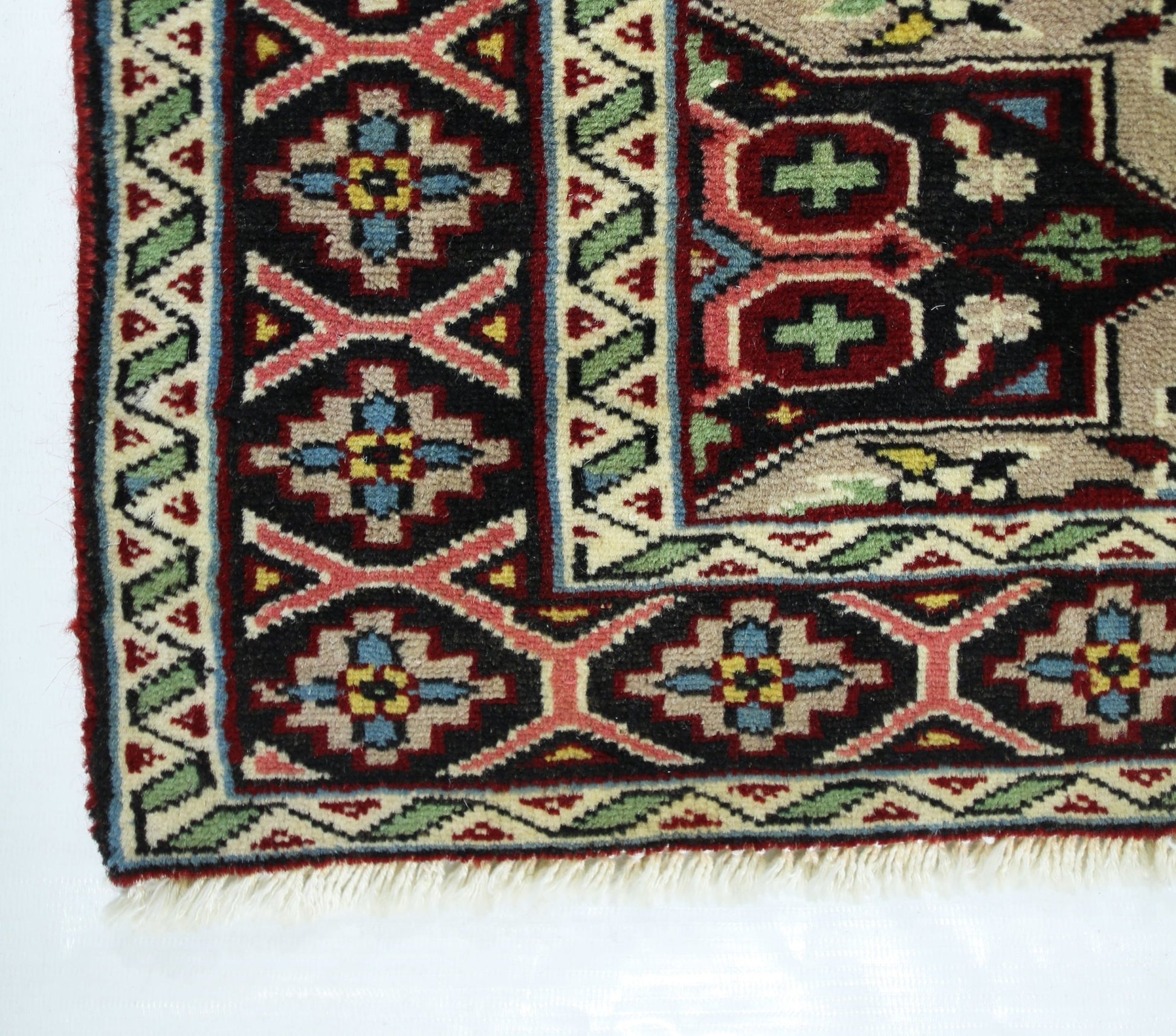 A corner view of a vintage Turkish prayer rug featuring geometric patterns in red, blue, and green.