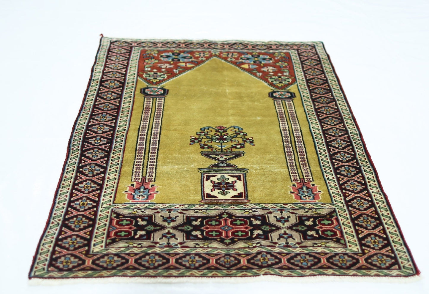 A vintage handmade Turkish prayer rug featuring a mustard yellow field with floral motifs.