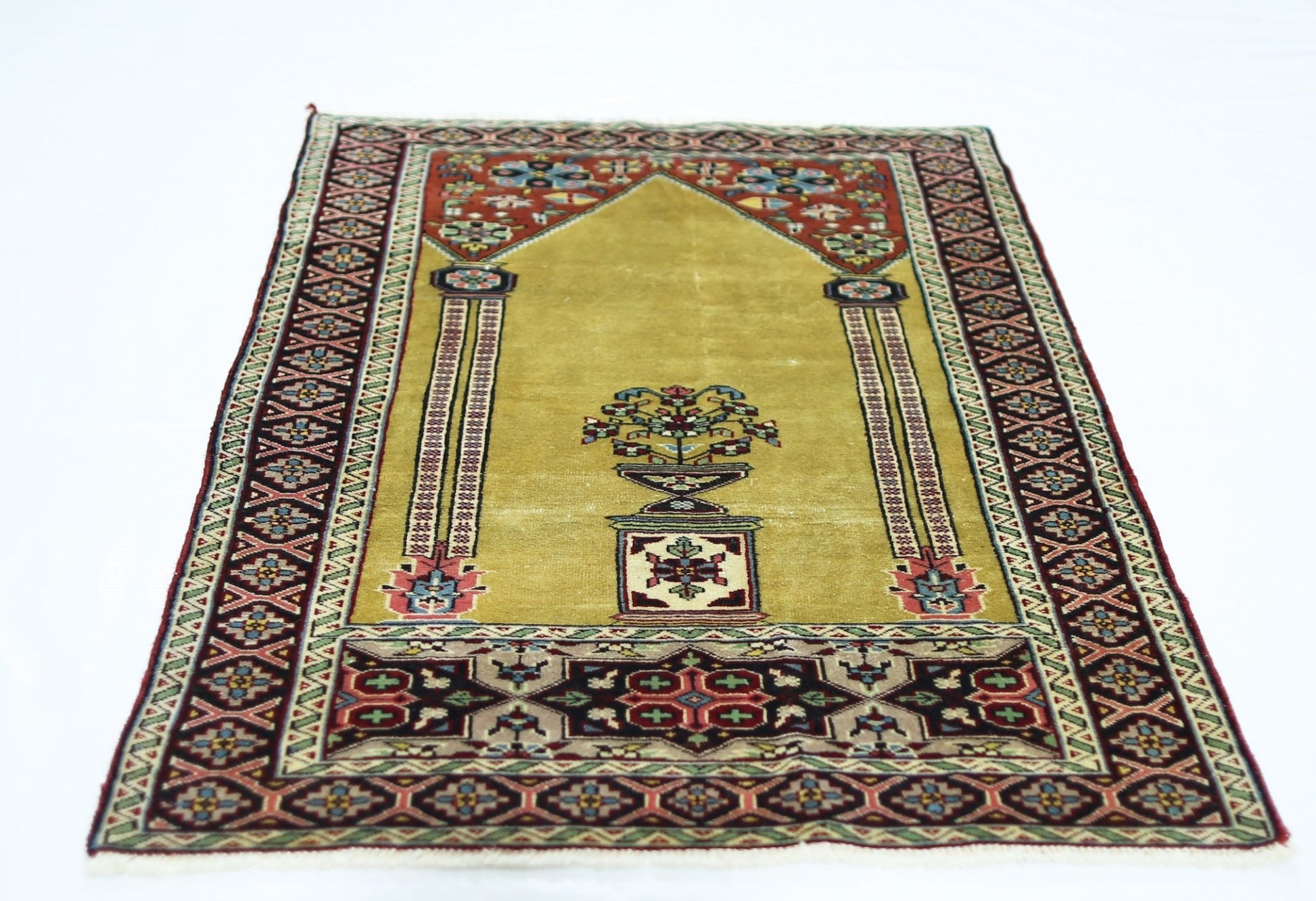 A vintage handmade Turkish prayer rug featuring a mustard yellow field with floral motifs.