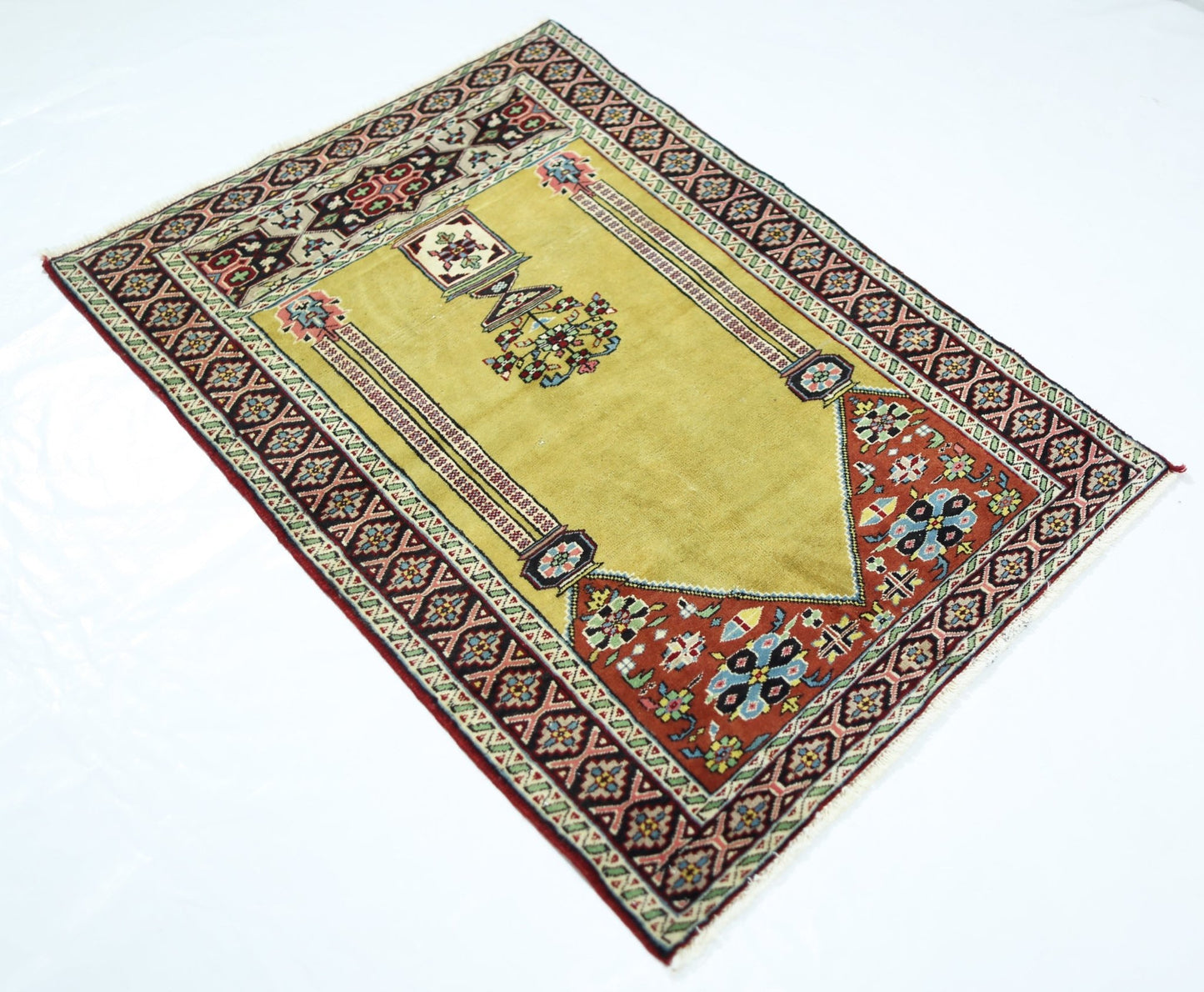 A vintage handmade Turkish prayer rug featuring a yellow mihrab design with floral motifs.