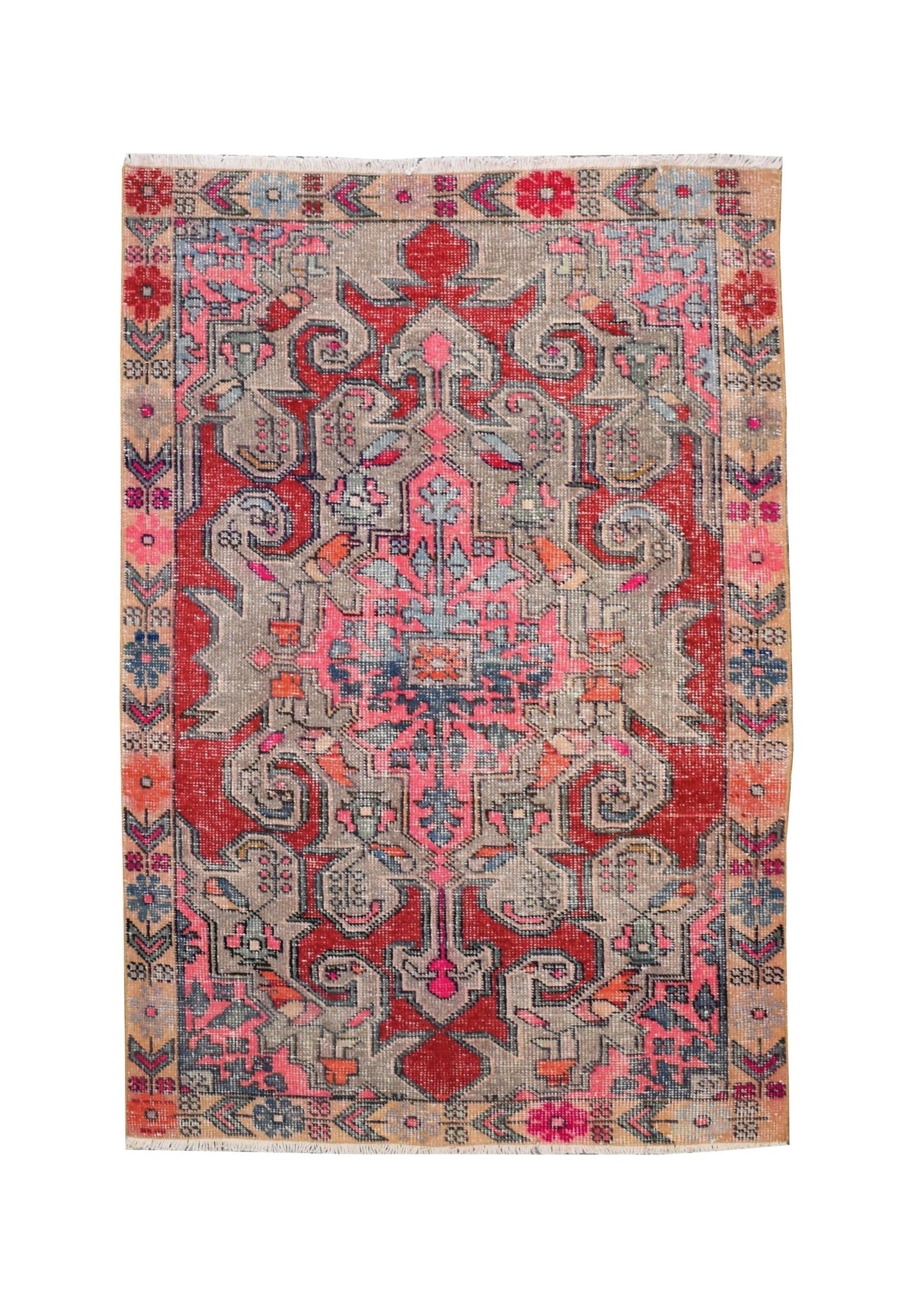 A vintage handmade Turkish wool rug featuring a geometric floral pattern in red, pink, and grey.