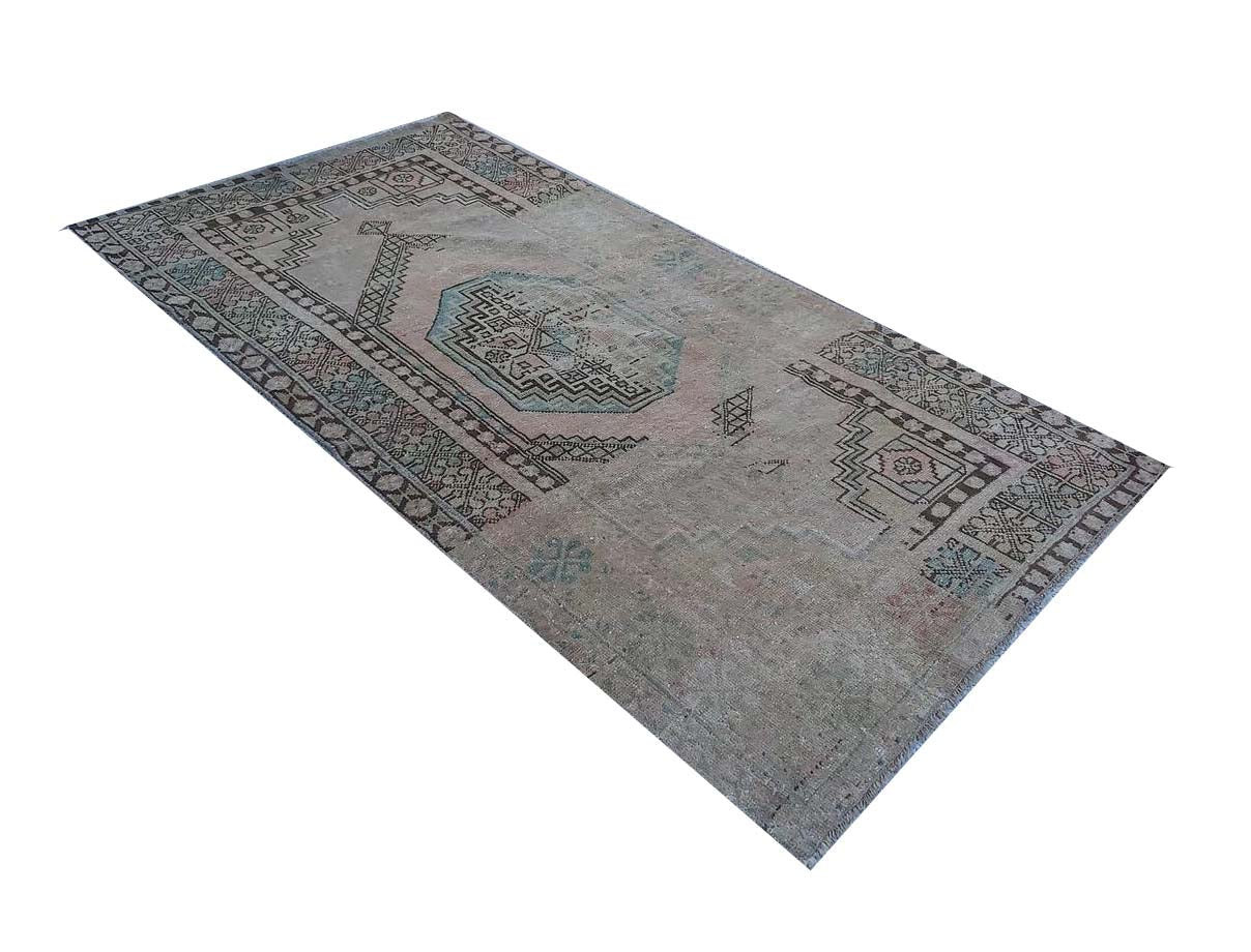 A vintage handmade Turkish wool rug featuring a faded geometric pattern in muted grey and blue tones.