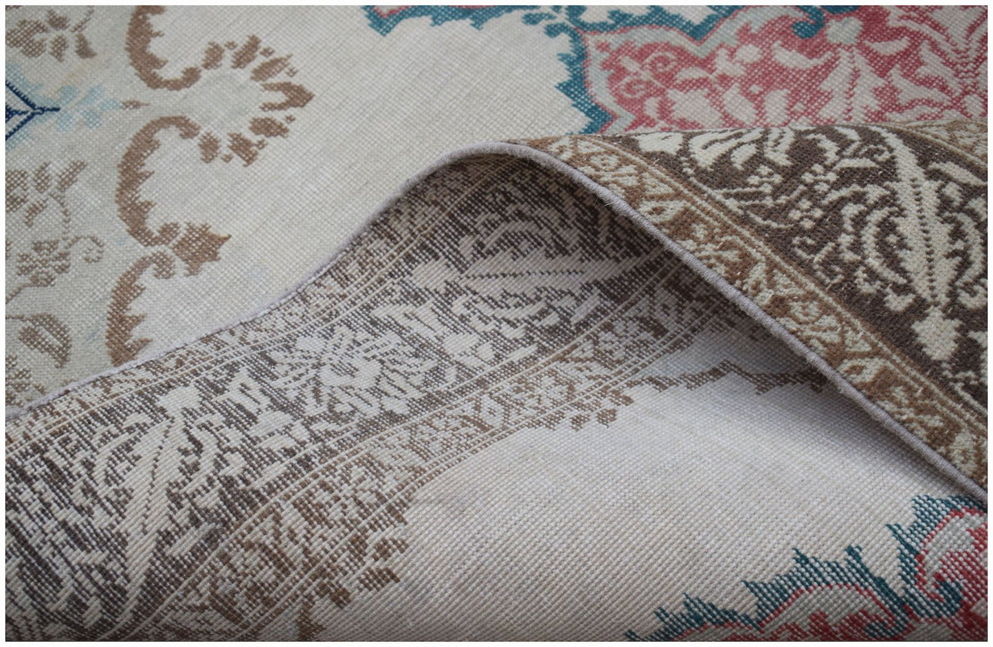 A vintage Turkish rug with a floral pattern in muted red, blue, and brown on a cream background.
