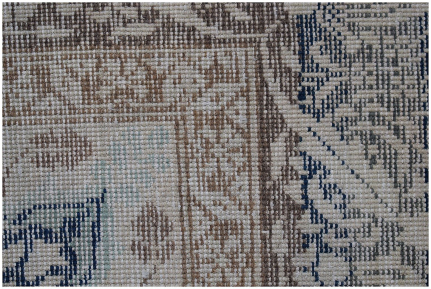 A close-up of a handwoven vintage Turkish rug featuring a geometric pattern in blue and brown.