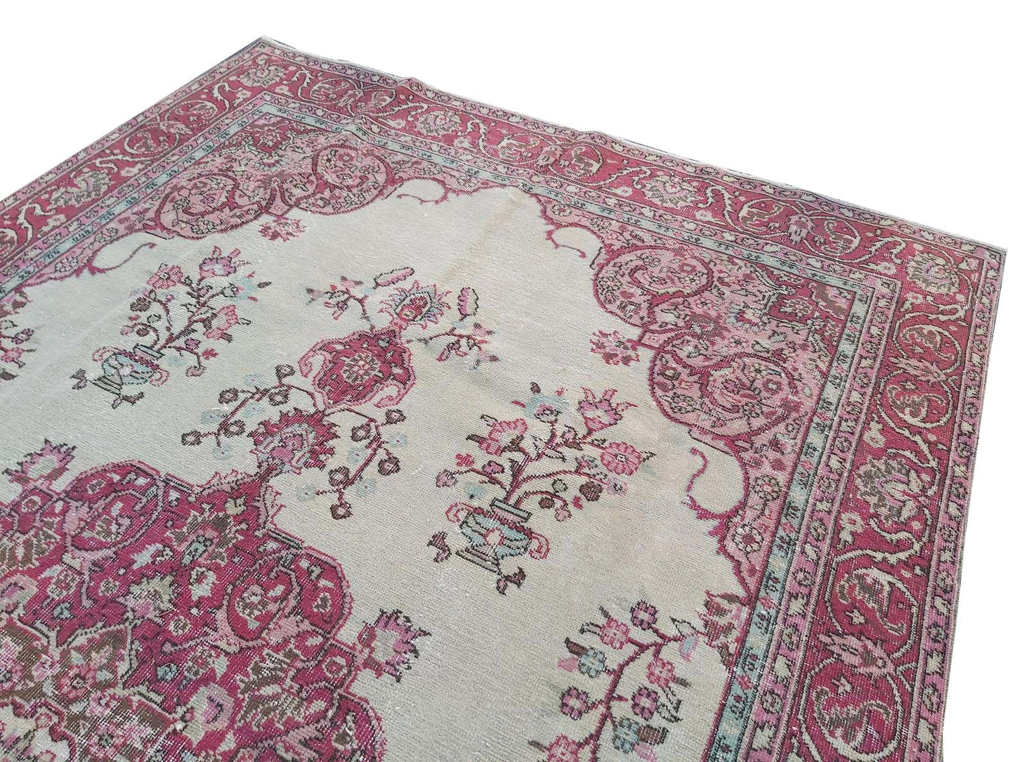 A vintage handmade Turkish wool rug featuring a cream field with pink floral and medallion motifs.