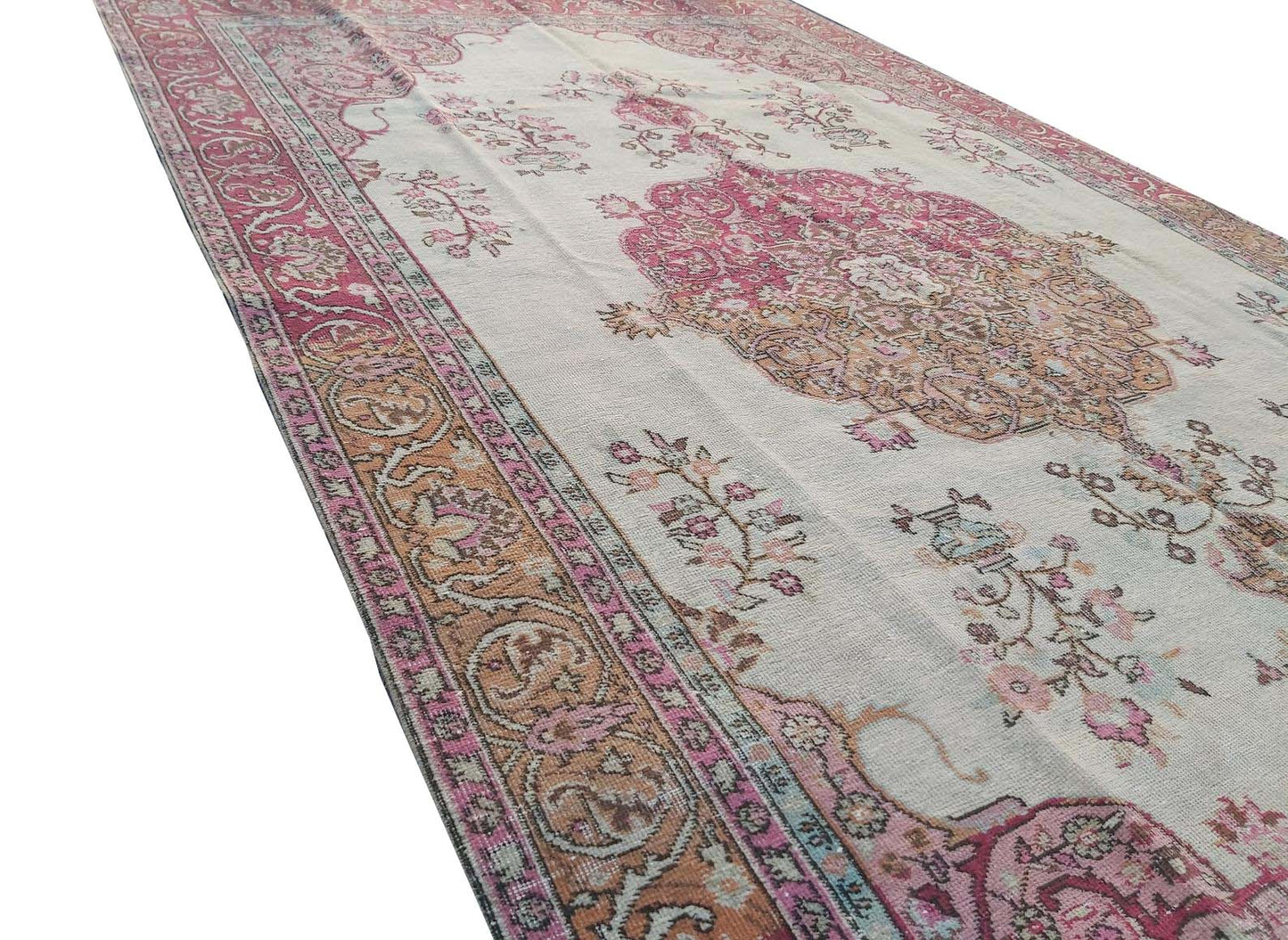A vintage handmade Turkish wool rug featuring a central medallion and floral motifs in pink and tan.