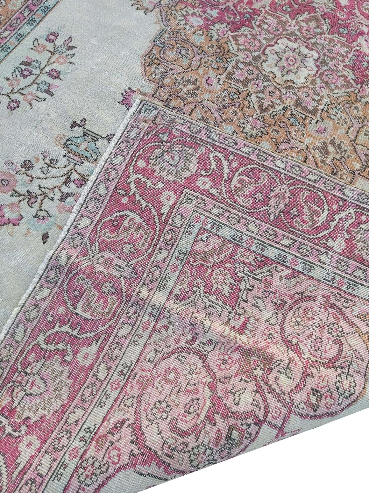 A vintage handmade Turkish wool rug featuring a pink and cream floral pattern.