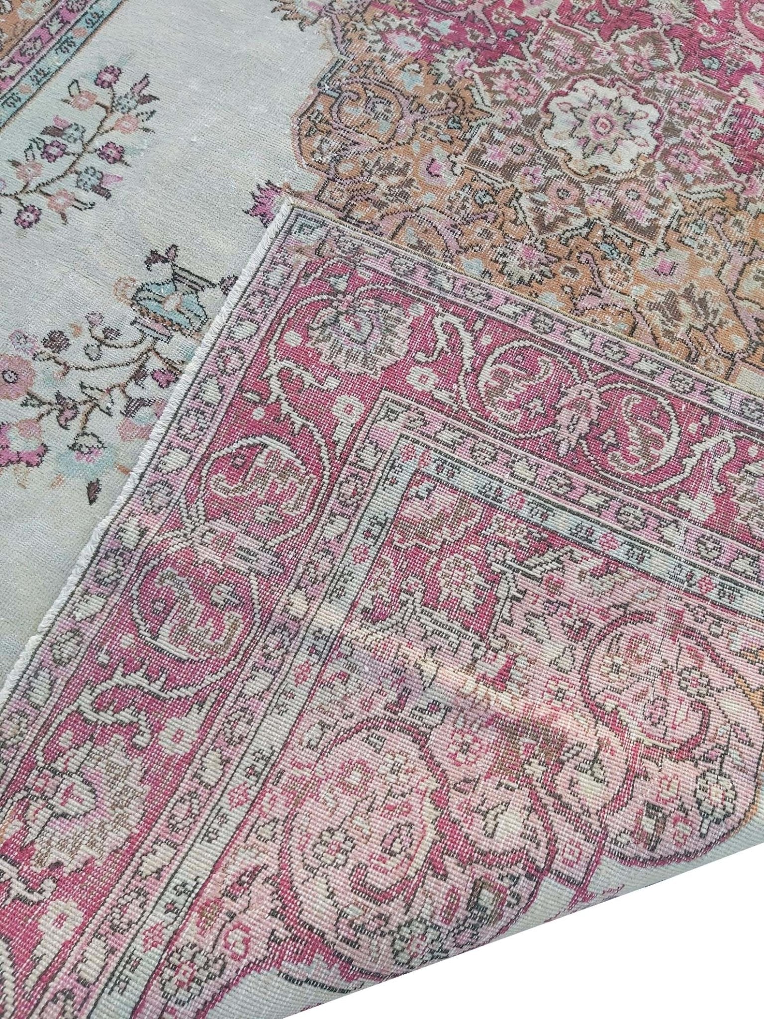 A vintage handmade Turkish wool rug featuring a pink and cream floral pattern.