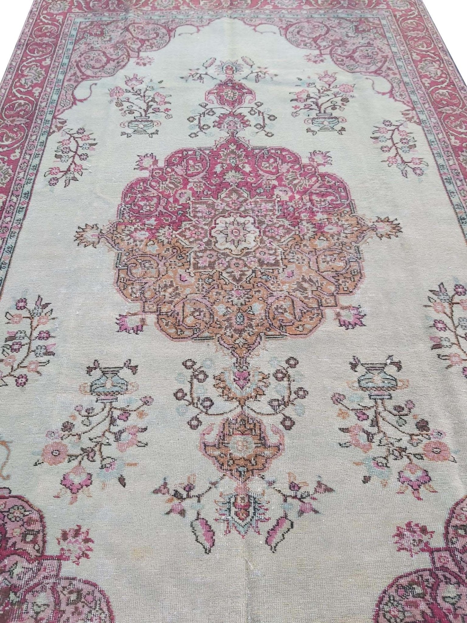 A vintage handmade Turkish wool rug featuring a central medallion and floral motifs in pink tones.