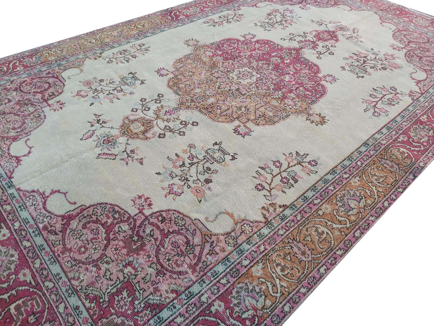 A vintage handmade Turkish wool rug featuring a central medallion and floral motifs in pink and tan.