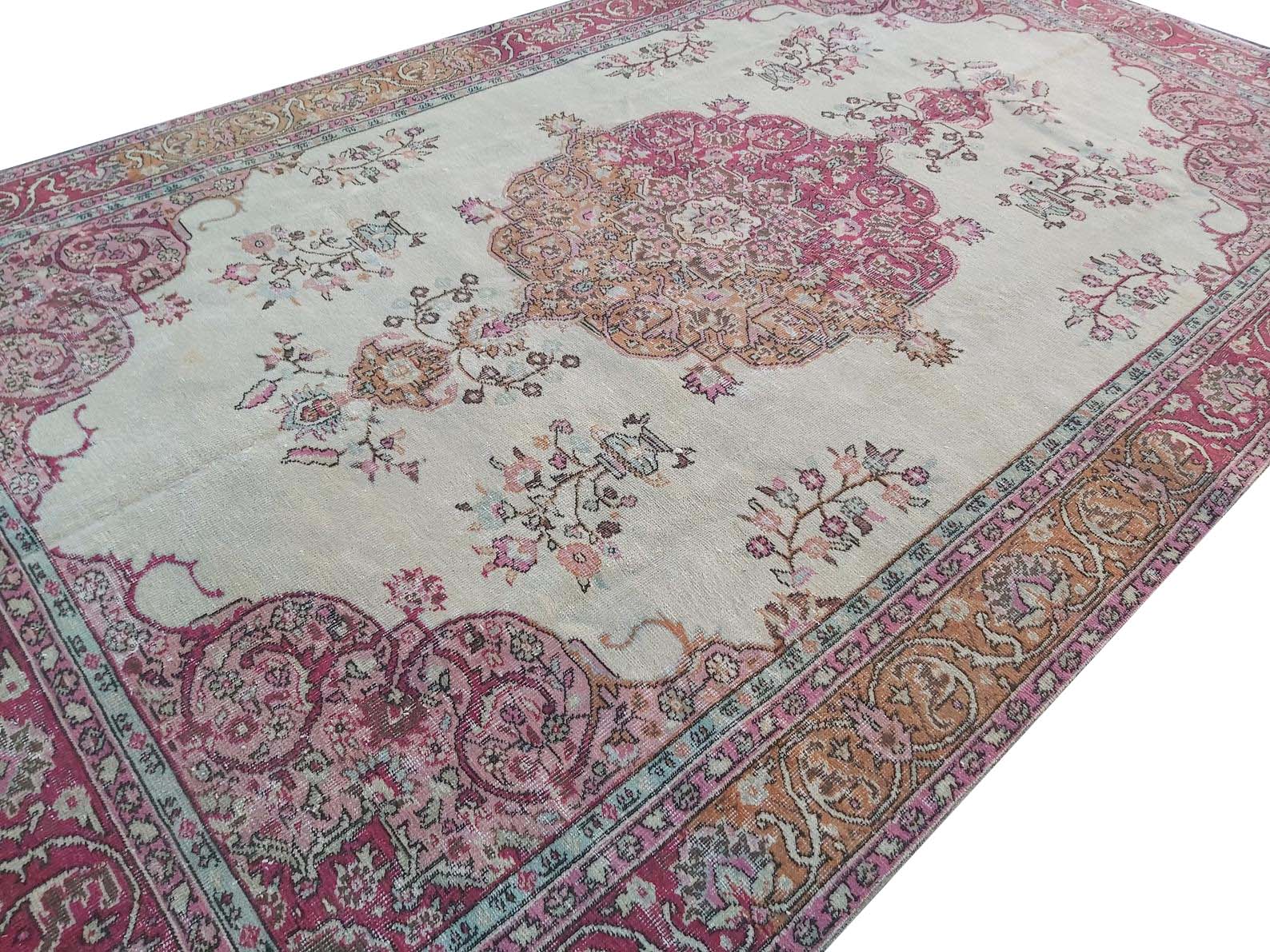 A vintage handmade Turkish wool rug featuring a central medallion and floral motifs in pink and tan.