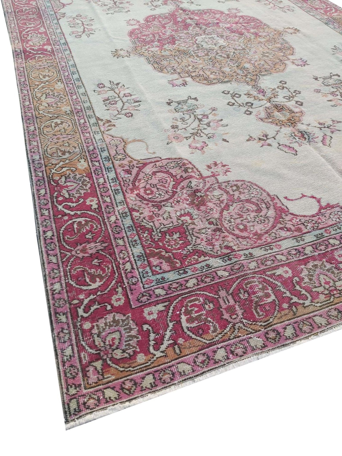 A vintage handmade Turkish wool rug featuring a pink floral medallion on a light cream background.