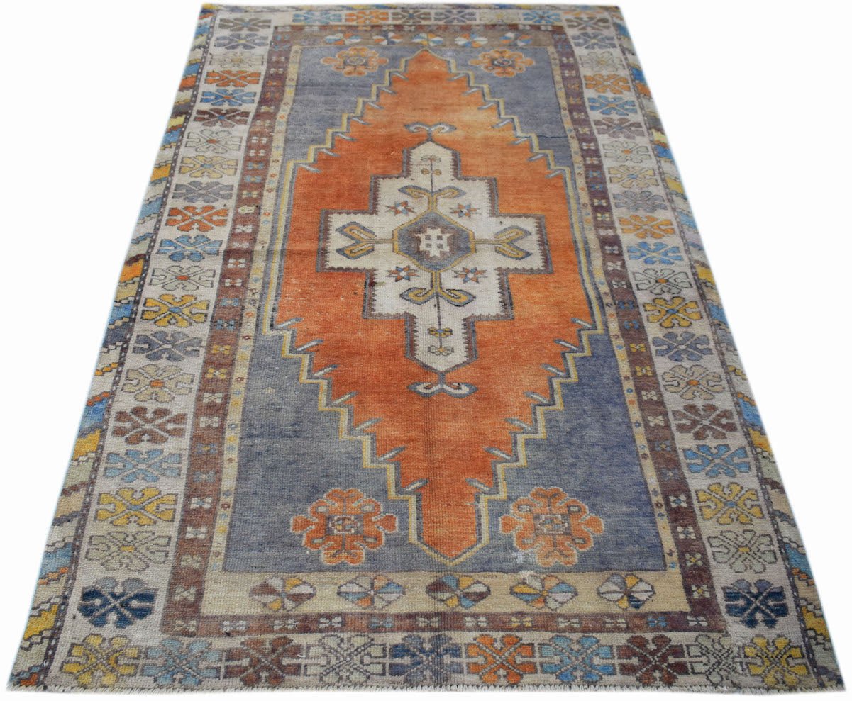 A vintage handwoven Turkish Taspinar rug featuring a central orange diamond on a blue field.