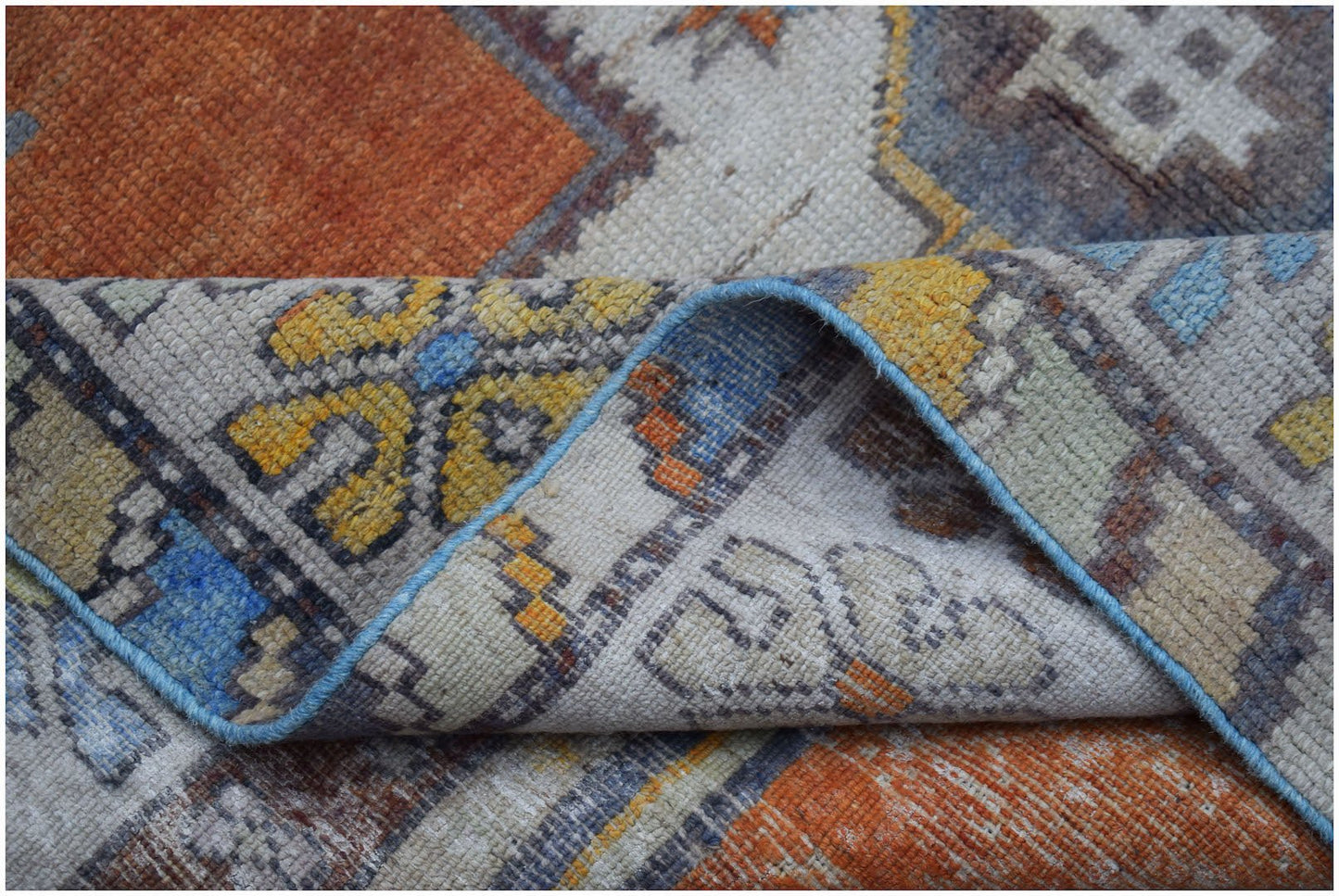 A vintage handwoven Turkish Taspinar rug featuring a geometric pattern in orange, blue, and yellow.