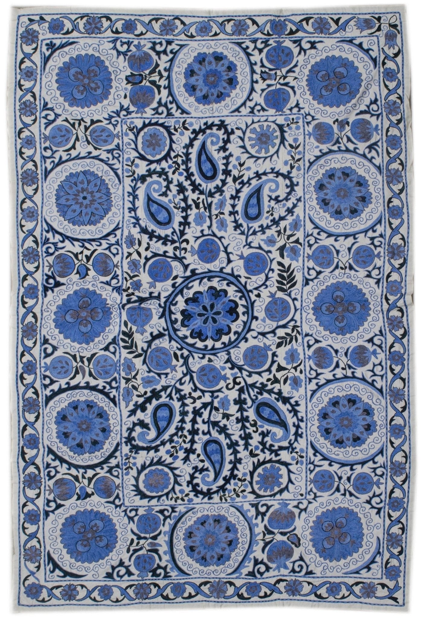 Handmade Uzbek suzani featuring blue floral and paisley embroidery on a white cotton base.