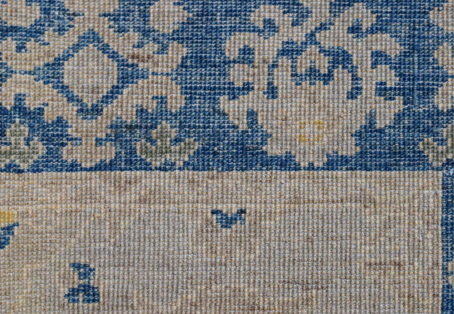 A close-up of an Afghan Chobi runner featuring a blue floral pattern on a beige wool background.