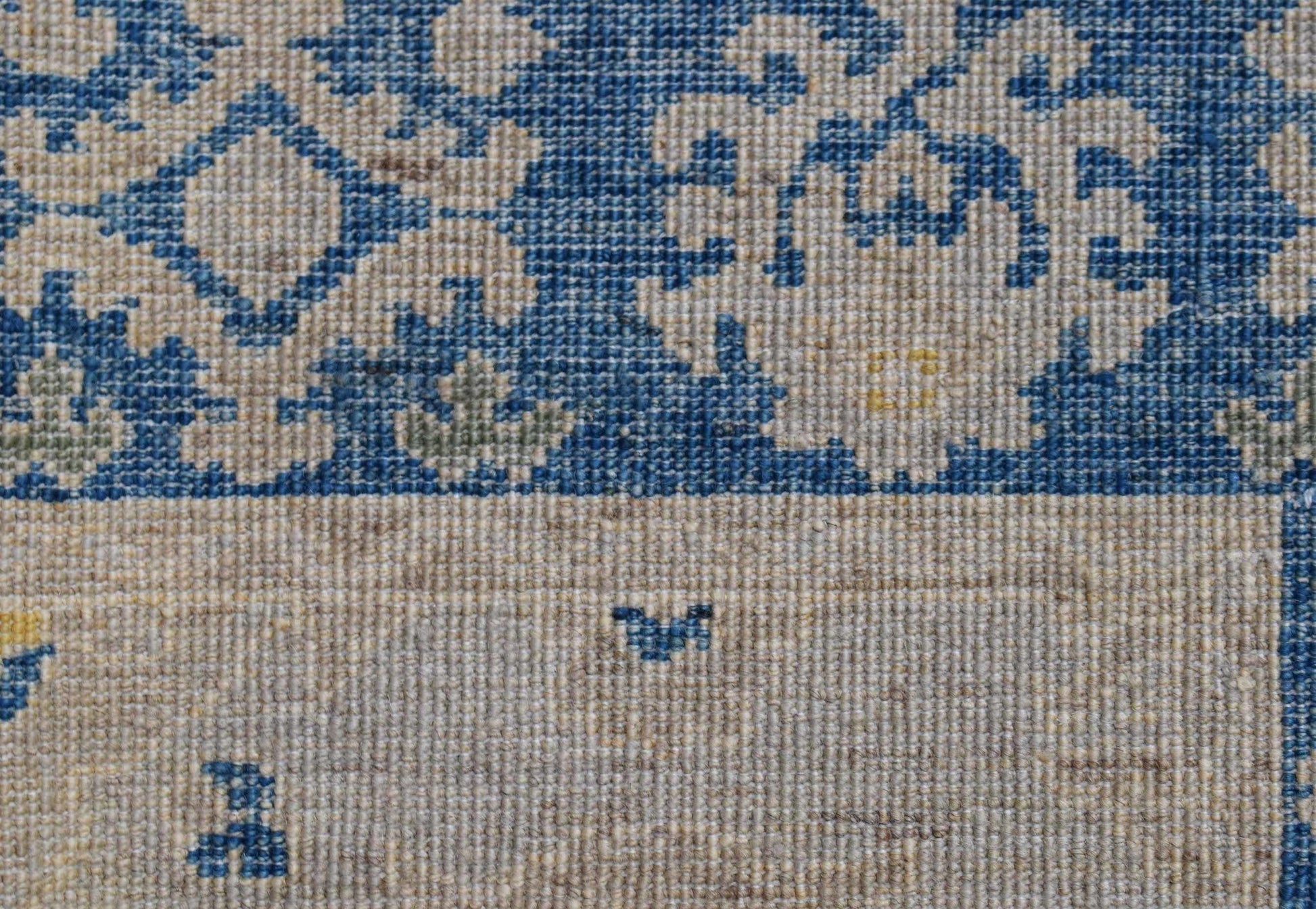 A close-up of an Afghan Chobi runner featuring a blue floral pattern on a beige wool background.