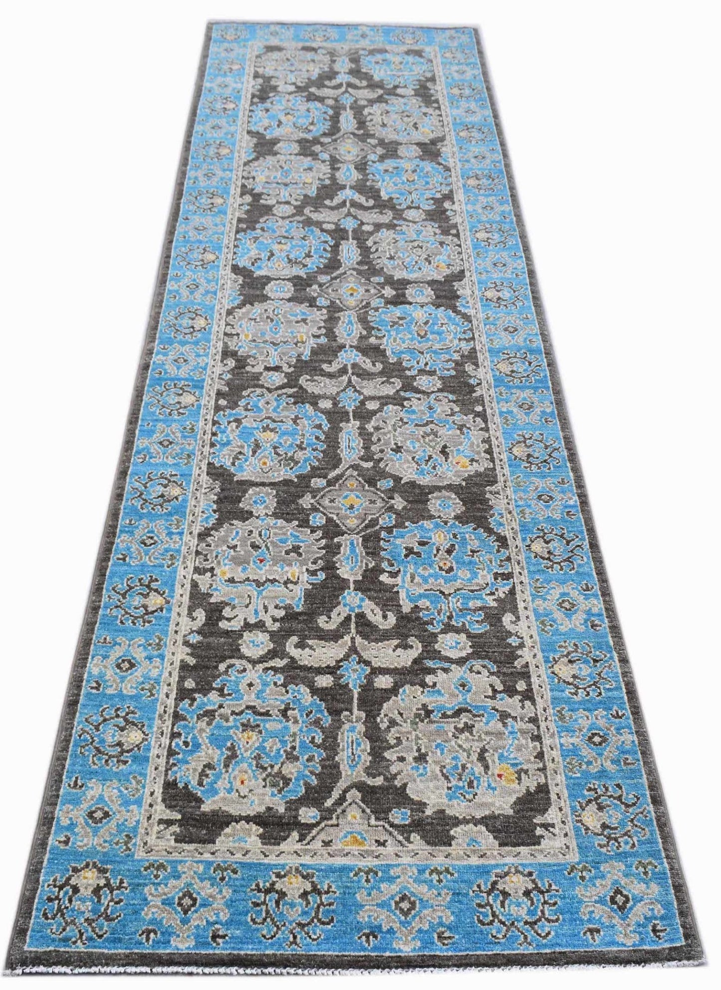 An Afghan Chobi runner rug featuring a dark brown field with intricate blue and grey floral motifs.