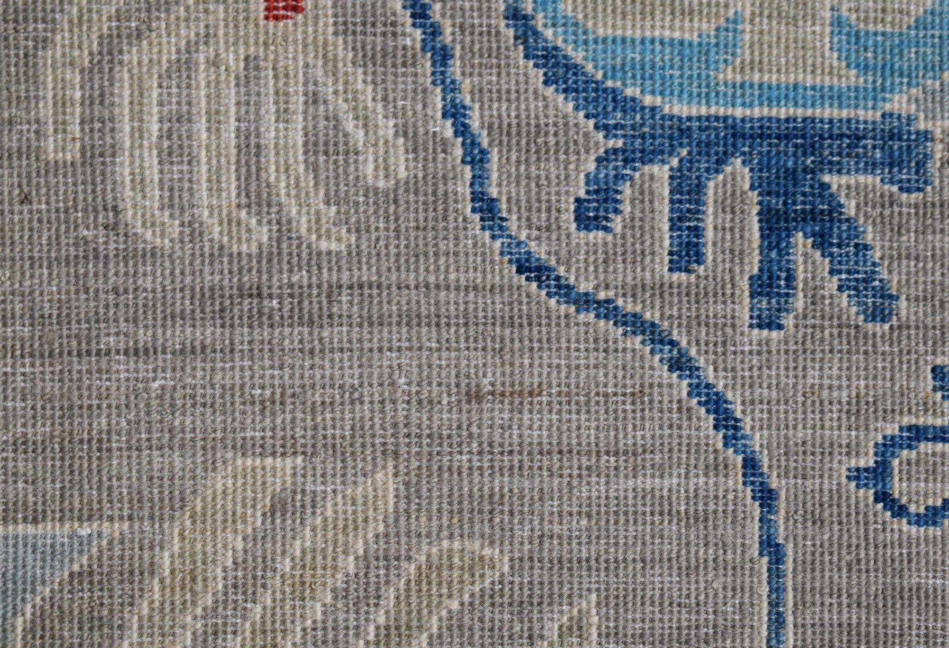 A close-up of a handwoven Afghan Chobi runner featuring blue floral patterns on a grey wool base.