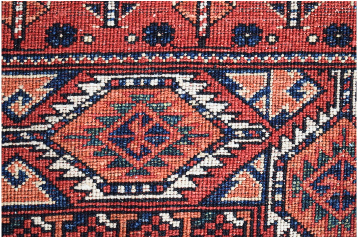 A close-up of a handwoven Afghan Chobi rug featuring geometric patterns in red, blue, and cream.