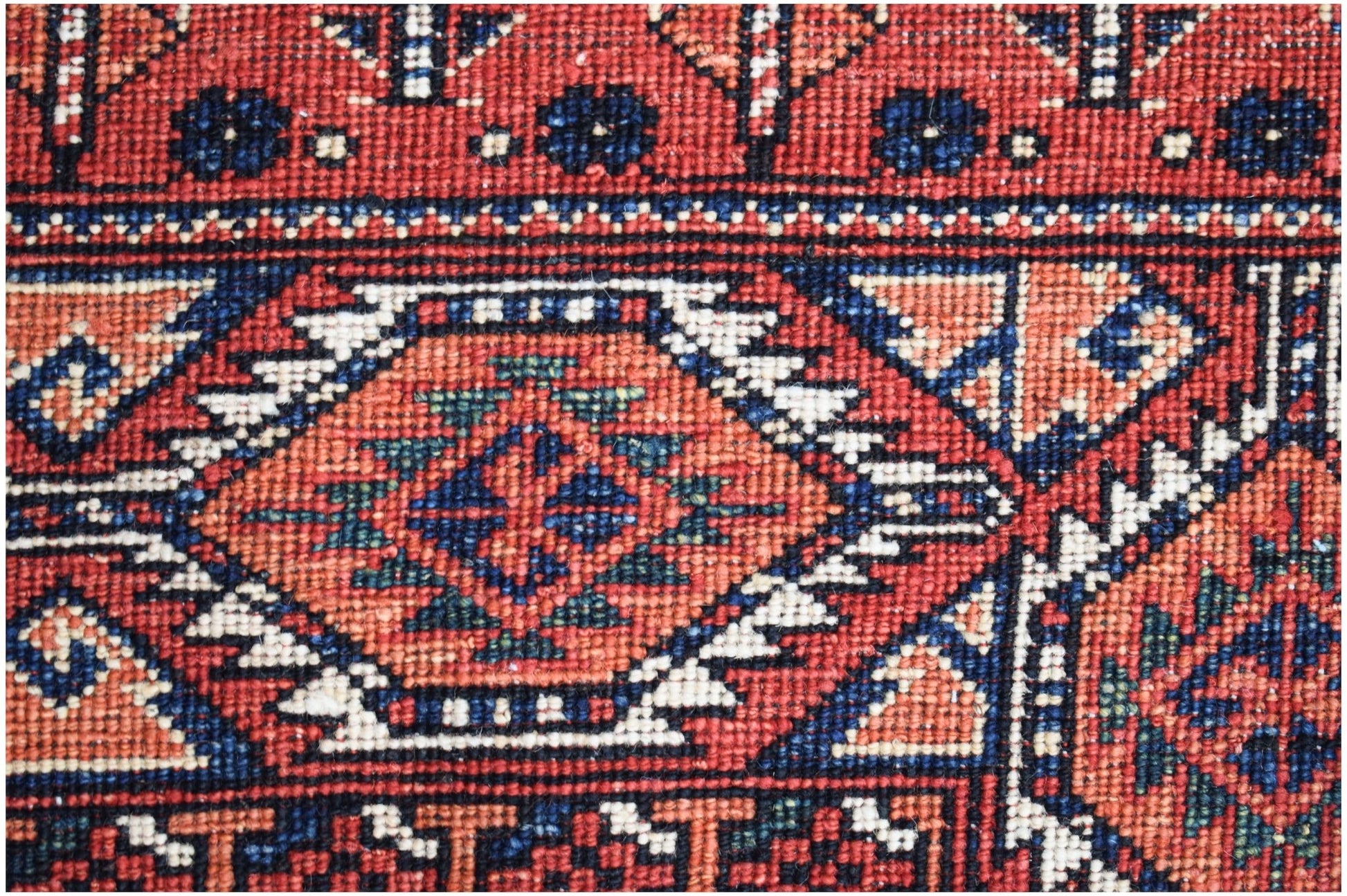 A close-up of a handwoven Afghan Chobi rug featuring geometric patterns in red, blue, and cream.