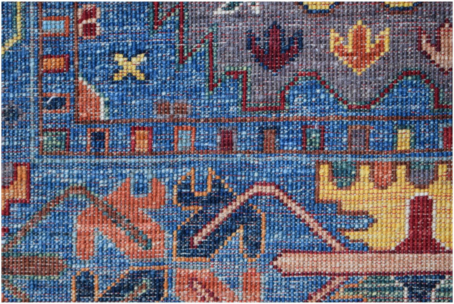 A close-up of a handwoven Afghan Chobi rug featuring intricate geometric patterns in blue and gold.